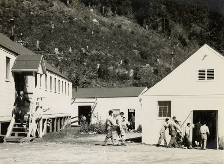 A black and white photograph of men walking outside of buildings at Kooskia. They appear to be walking between two buildings.