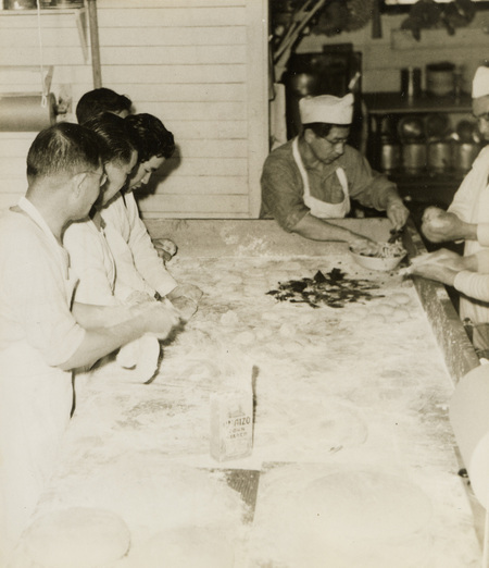A black and white photograph of men working with flour at a large table.