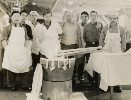 A black and white photograph of men in front of an usu that was used to make mochi. There are eight men posing for the photograph.