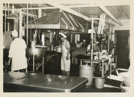 A black and white photo of a kitchen and men working.