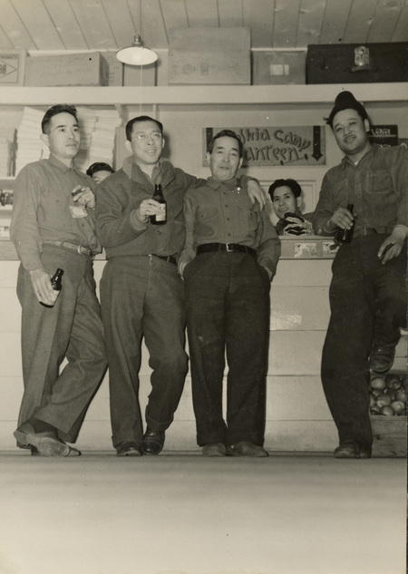 A black and white photograph of a group of men sitting in front of a counter and drinking beverages.