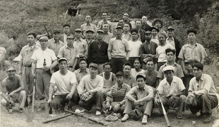 A black and white photograph of a baseball team. Baseball bats are balanced at the front and center of the group.