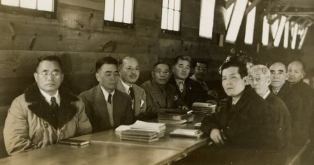 A black and white image of a large group of men sitting at a table, presumably for a meeting. 
