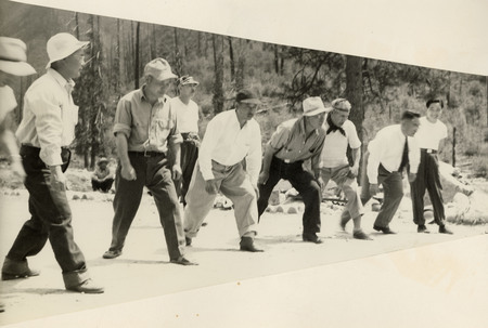 A black and white photograph of a footrace. Seven men stand in a line preparing to run.
