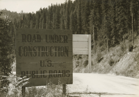 A black and white photograph of a sign. The text reads "Road Under Construction. U.S. Public Roads".