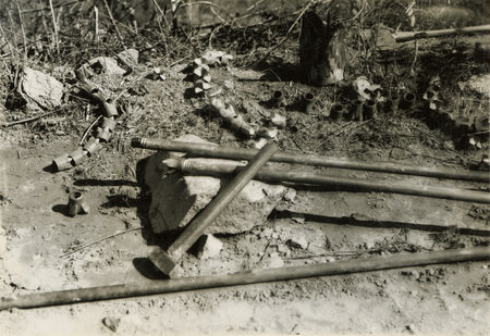 A black and white photograph of four pipes on the ground. Other metal parts are on the ground next to the pipes.