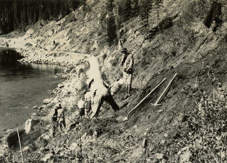 A black and white photograph of men digging along a hillside with pickaxes and shovels.