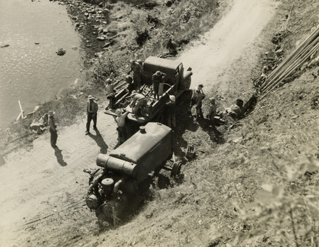 A black and white photograph of men unloading construction tools and equipment from a truck on a dirt road.