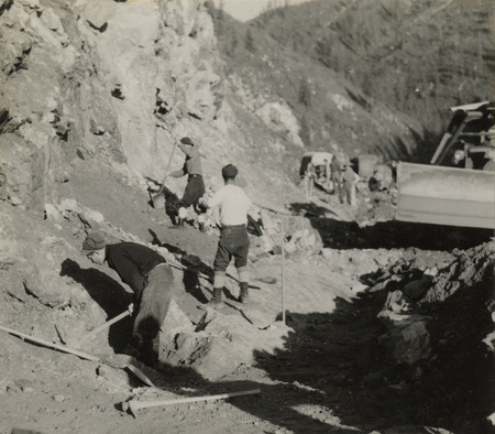 A black and white photograph of men working along a hill side with pickaxes and shovels.