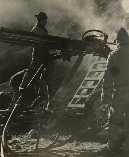 A black and white photograph of three men working with construction equipment.