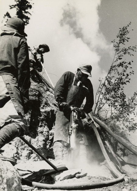 A black and white photograph of three men using a jackhammer and other construction equipment.