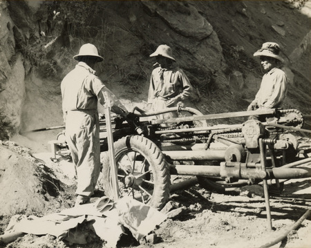 A black and white image of three men standing next to construction and drilling equipment.