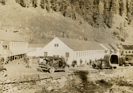 A black and white photograph of vehicles in front of buildings next to the river.