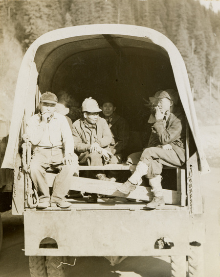 A black and white photograph of men sitting in the back of a transport vehicle.