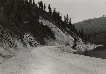 A black and white photograph of a gravel road along a river.