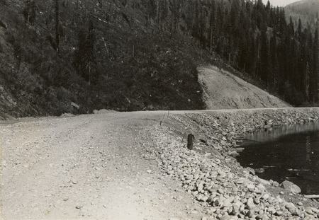 A black and white photograph of a gravel road along a river.