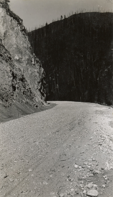 A black and white photograph of a gravel road along a river.