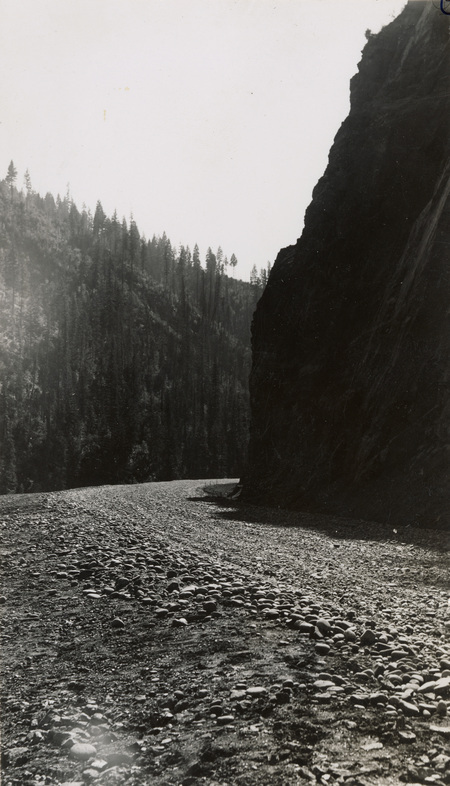 A black and white photograph of a gravel road along a river.