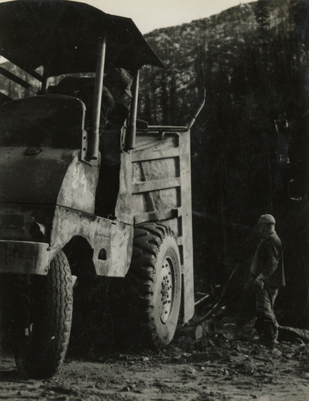 A black and white photograph of two men working with a dump truck.