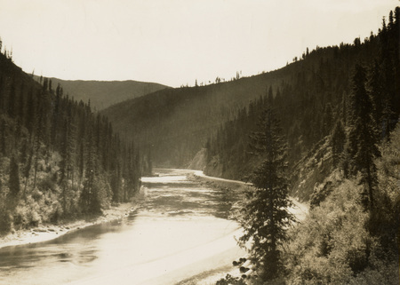 A black and white scenic photograph of a river. Pine trees line the river's edge.