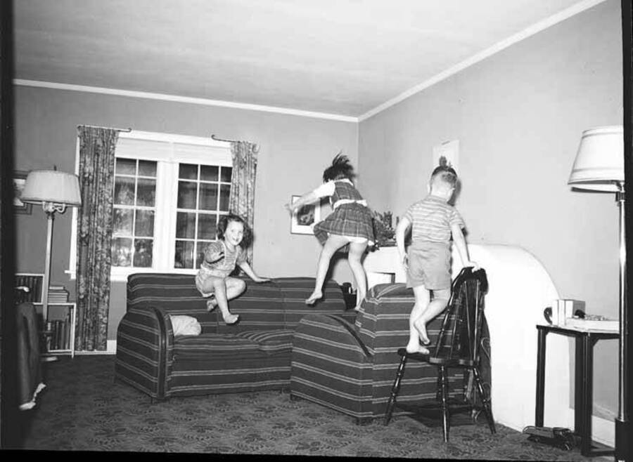 Image shows John, Helen and Kay Laughlin jumping on furniture in the living room.