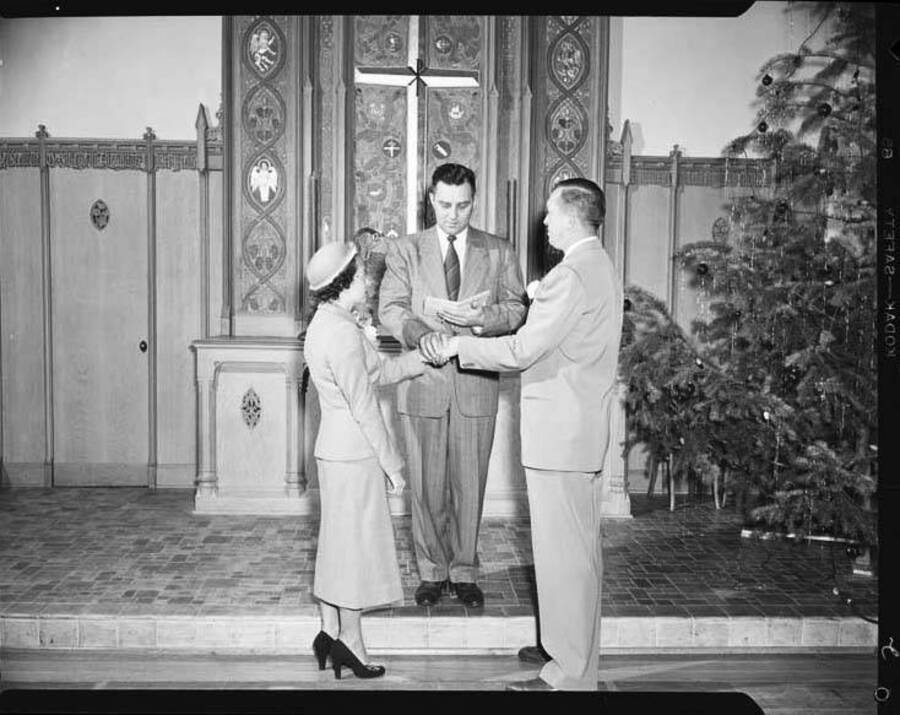 Image shows Don Wilson and his bride standing before the minister in a church on their wedding day during Christmas time.