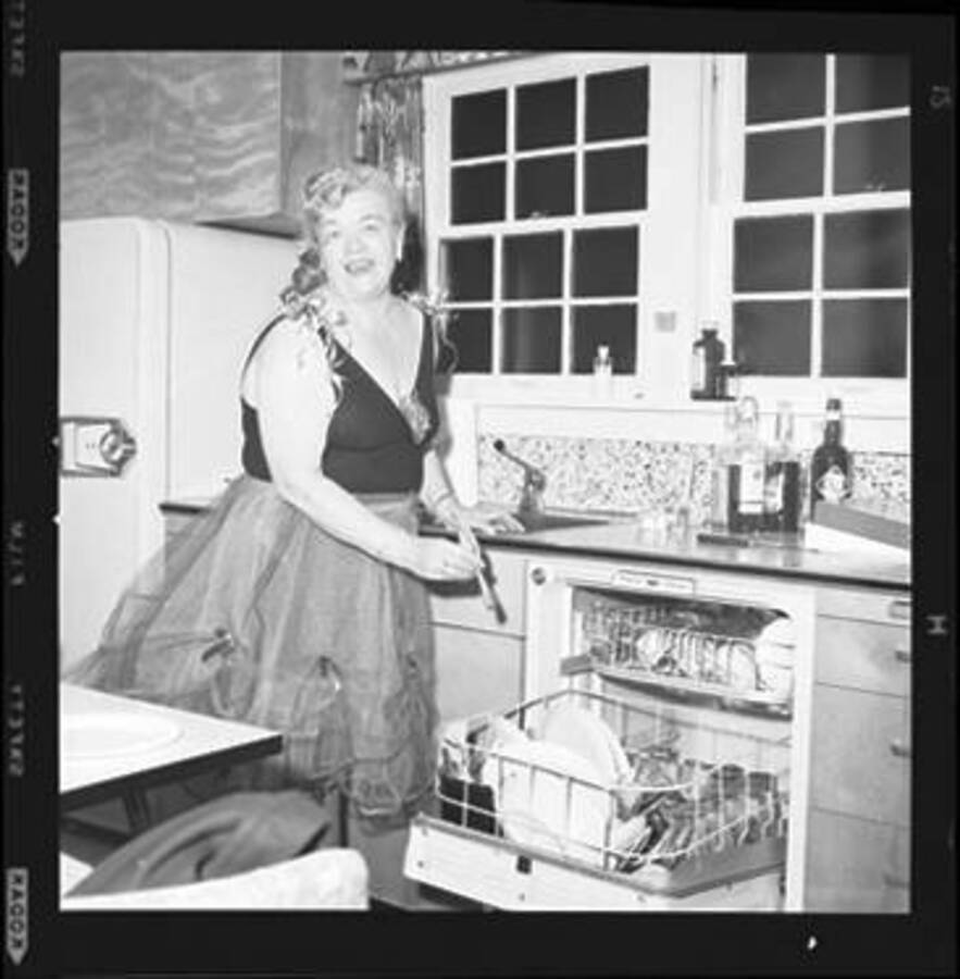Woman in costume in a kitchen putting dishes in a dishwasher.