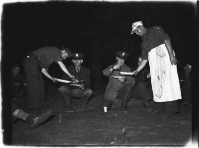 An evening image of National Guardsmen eating dinner in a wooded area on a  trip.