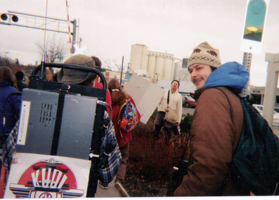 Protesters walking from the University of Idaho to the courthouse during the anti-war rally in 1998. One man walks next to another man wearing the KUOI transponder unit.
