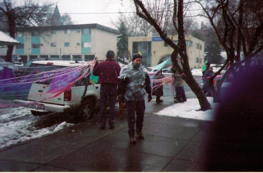 A man is wrapped in duct tape at the Code Pink War Protest in February 2003. Pink ribbons and people holding signs can be seen in the background.