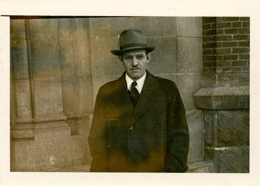 Bert Hopkins standing in front of a brick academic building, wearing a hat and overcoat
