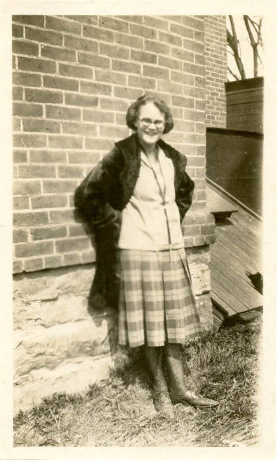 Photograph of an unknown woman leaning on a brick building, presumed to be on campus