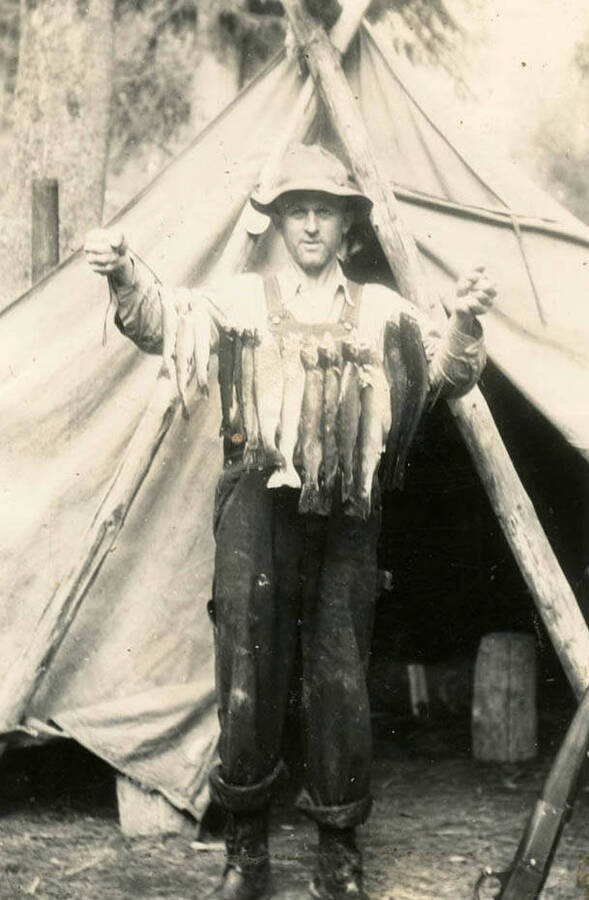 Eddie standing outside of a tent holding a line of fish he caught .