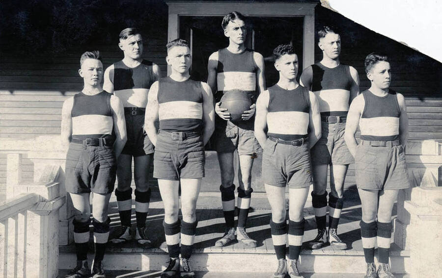 Postcard of high school men's basketball team taken in front of the old gymnasium. The name Chuck Johnson is on the back.