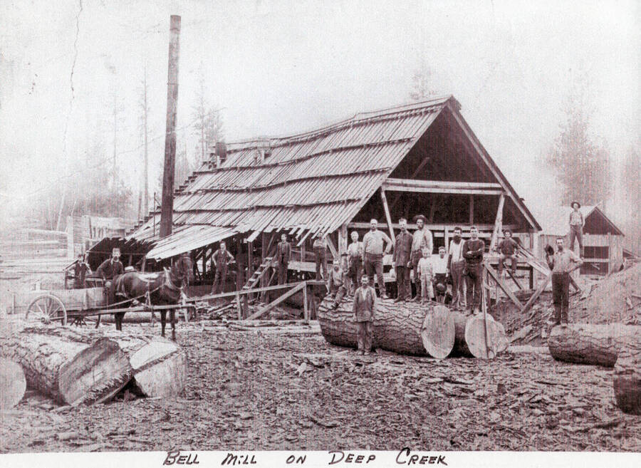 The Bell Mill on Deep Creek. A group of men can be seen standing on and around logs in front of a structure.