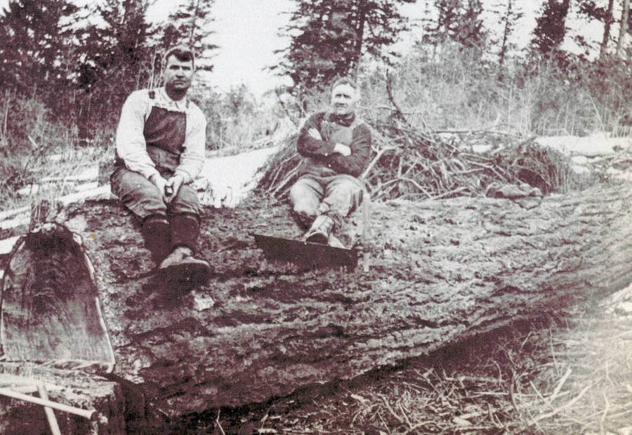 Amos Grate and John nirk sitting on a fallen log.