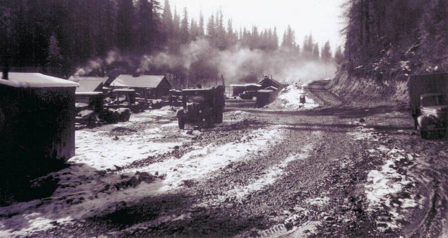 Camp 36 logging camp with trucks and tents. Smoke can be seen coming from the chimneys in the tent structures.