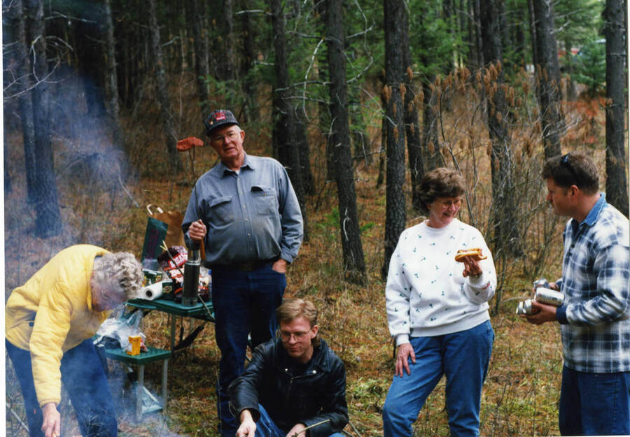The Daniels family enjoying a picnic while out cutting down the Christmas tree as per tradition. Individuals identified by activity and clothing: Wiley Daniels with stick, son Lawrence Daniels sitting down, Aunt Monty in yellow, Wilma in sweatshirt, Johann at right.