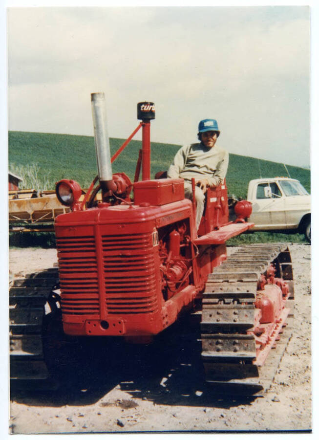 Phil Fleener atop TD6 International Harvester tractor. Note previous owner's modification of adding a turbocharger to the top of the tractor's hood. Palouse farmers would modify tractors that were orignally intended for flat land farming to adapt them for the rolling hills. Barber Engineering dry fertilizer spreader in background.