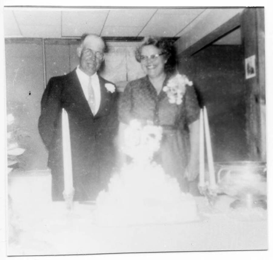 Vernon and Alice Briney posing for photos in front of their cake at their 25th anniversary celebration.