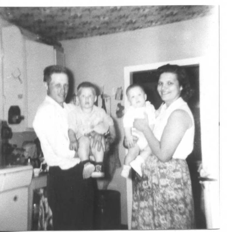 Photo of the Fleener family while standing in a kitchen. The parents are seen holding the children. Names read as subjects appear, left to right: Fleener, Loyal Ivan; Fleener, Craig Loyal; Fleener, Timothy Paul; Fleener, Marva Joyce.