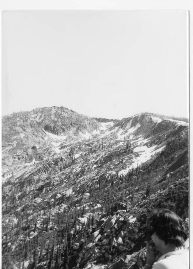 View of a mountain on the Fleener family Selway trip. Marva Joyce Fleener can be seen in the foreground. Warren Hill offered Fleeners the use of his cabin one summer.