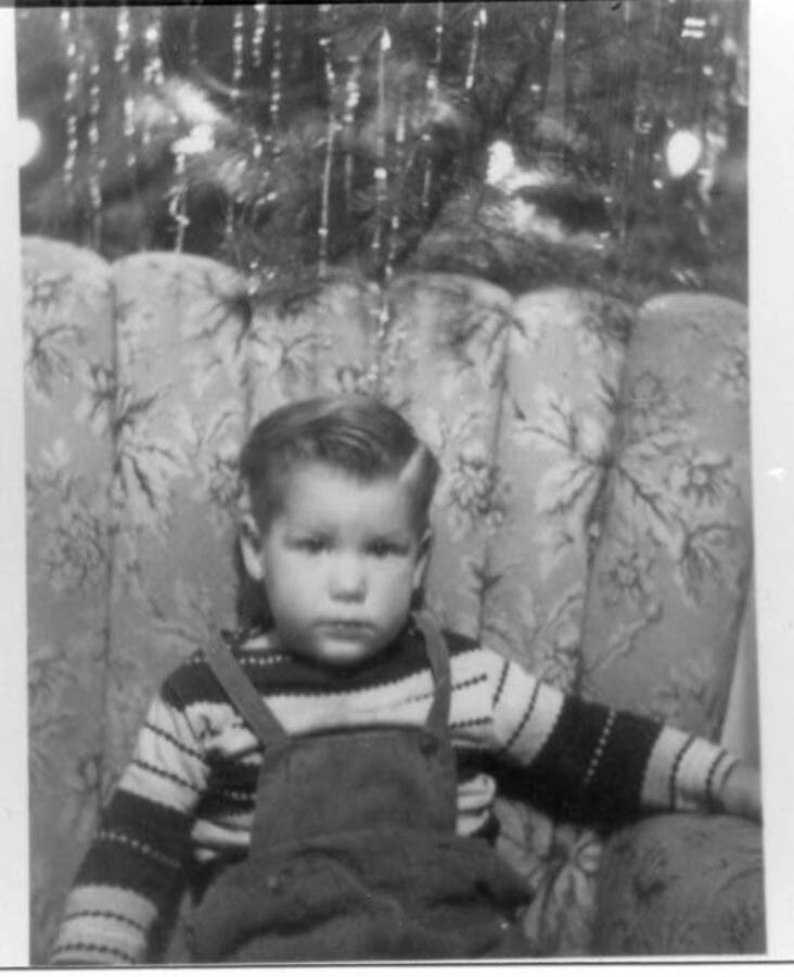 Tim Fleener posing for a Christmas photo. A Christmas tree can be seen standing behind the chair he is sitting in.
