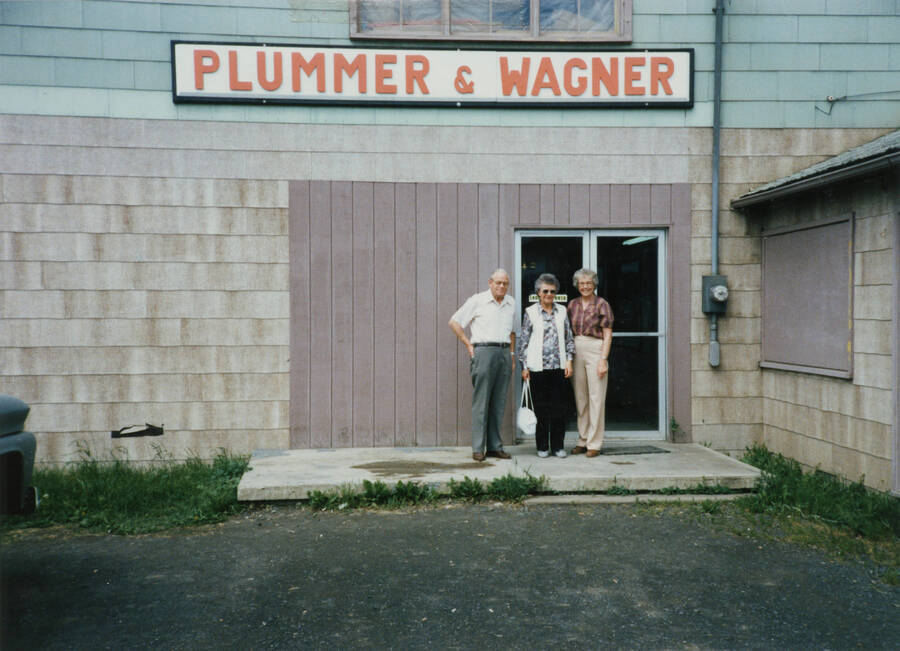 Photo of (left to right) Velma Krasselt, Cleora Strong, and Dwight Strong in front of the Plummer-Wagner Lumber building. May 15, 1987