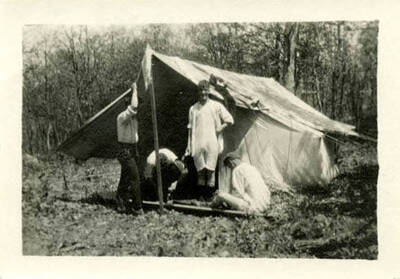 Bert Hopkins with friends camping in Latah County. Two of the men are in their undergarments, while one man is standing in suspenders and trousers.