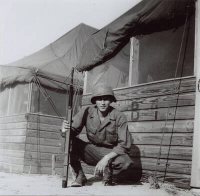 Norman Soncarty posing with a rifle next to the army barracks in Korea.