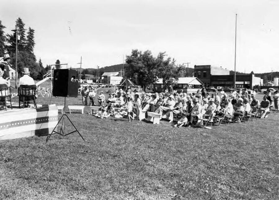 An audience listens to a speaker on a stage during Bovill's Statehood Day while children play in the front.