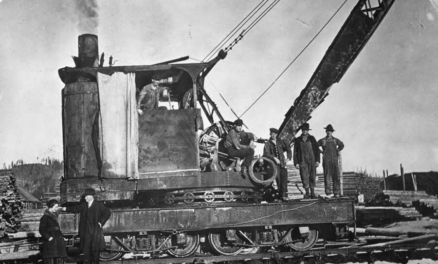 Men pose for a picture on a machine in the pole yard. Bill Melow (operator), Fred Wallen, Wandke, Heidke, Betty Helmier.