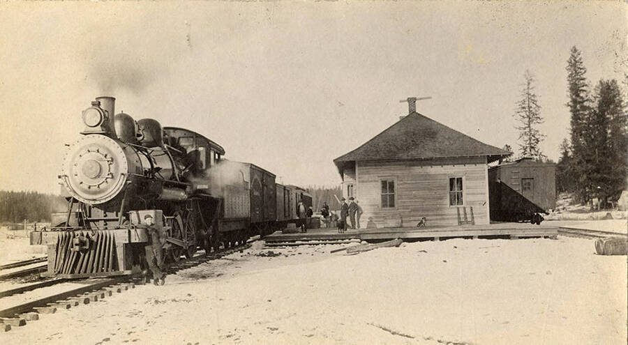 People stand at the Washington, Idaho, and Montana Rail Road Depot while the train waits.