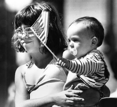 Jessica Paterek holds Jared Staniford, who is waving a flag, during Bovill's Statehood Day celebration.